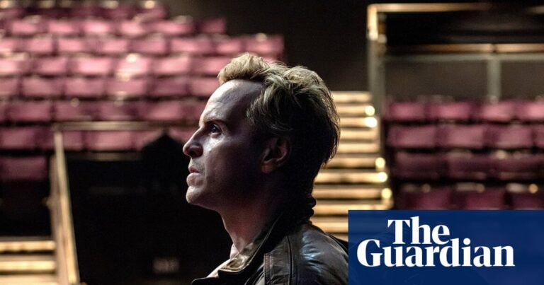 Andrew Scott, in a leather jacket, stands in profile looking upward inside an empty theatre